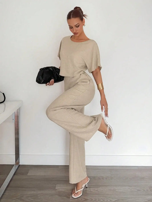 Woman in beige outfit posing indoors with a white wall background