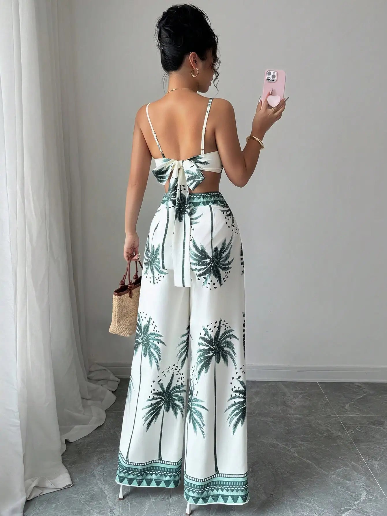 Woman wearing a white dress with green palm tree patterns, taking a mirror selfie.